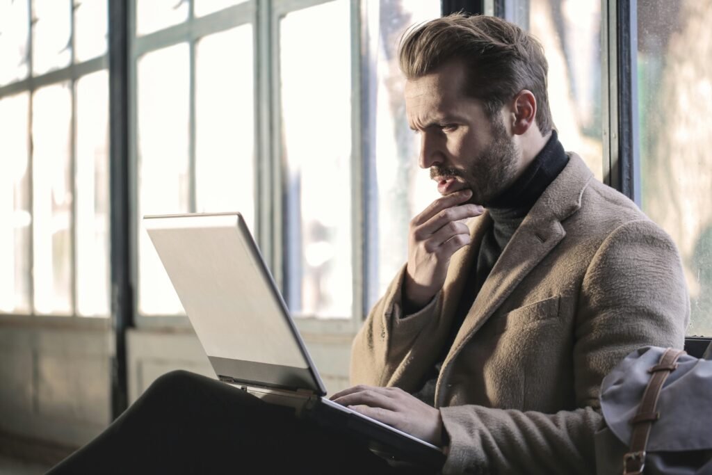 Man thinking by a window while planning on his laptop